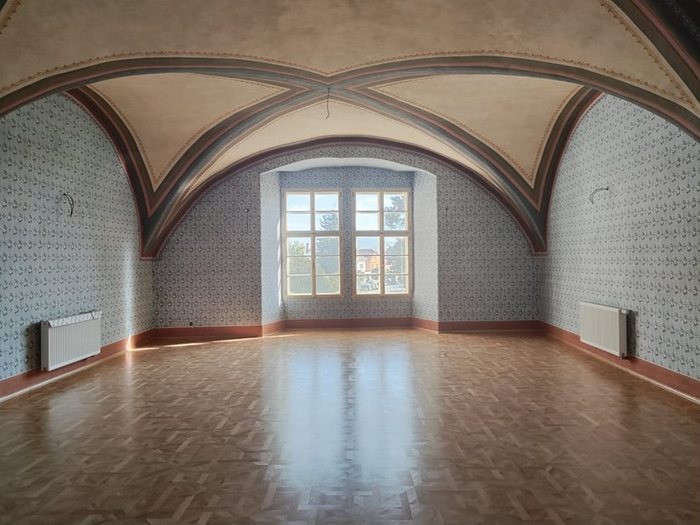 Obřadní sál po restaurování: malovaná žebra kleneb, šablonová malba stěn a lesklá parketová podlaha, pohled k oknu