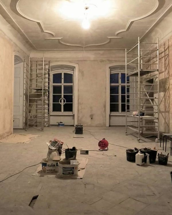 Táž místnost během prací: holé stěny i strop s rámovým polem, dvě pojízdná lešení, kbelíky a nářadí na podlaze